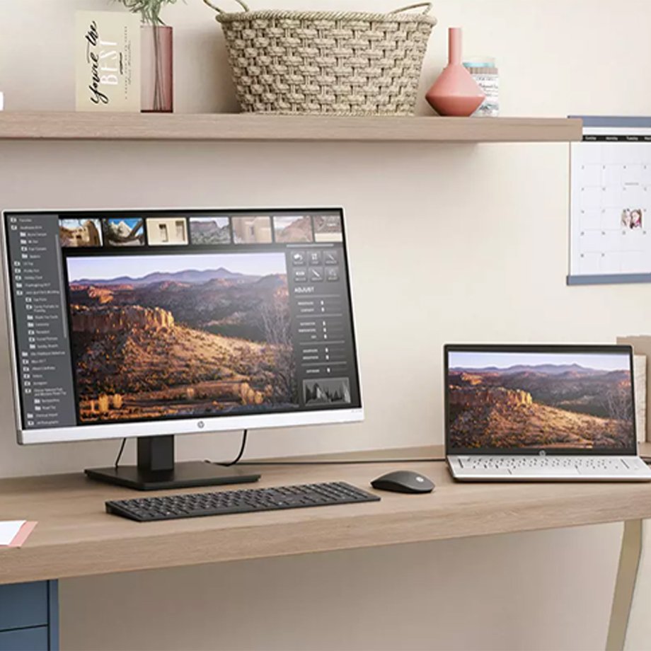 An HP PC placed next to an HP laptop on a wooden desk.